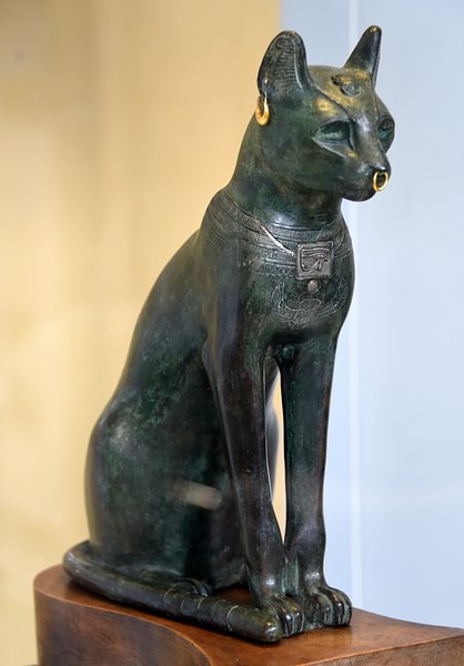A statue of Bastet in full cat form on all fours with gold jewelry. 